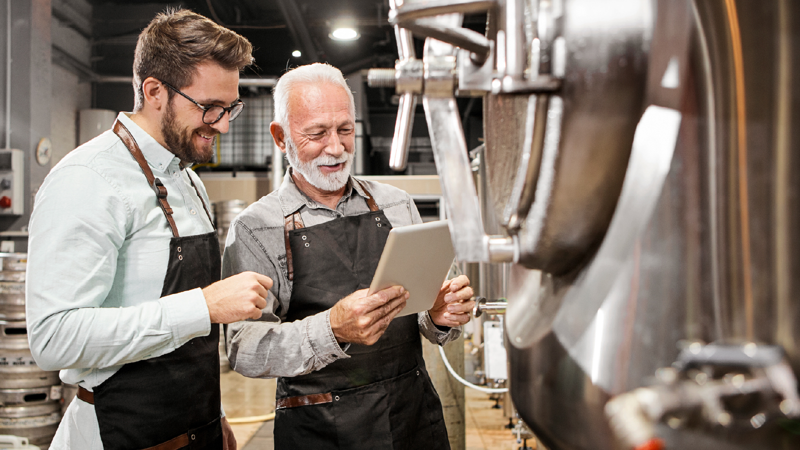 Two men wearing leather aprons inspecting brewing equipment