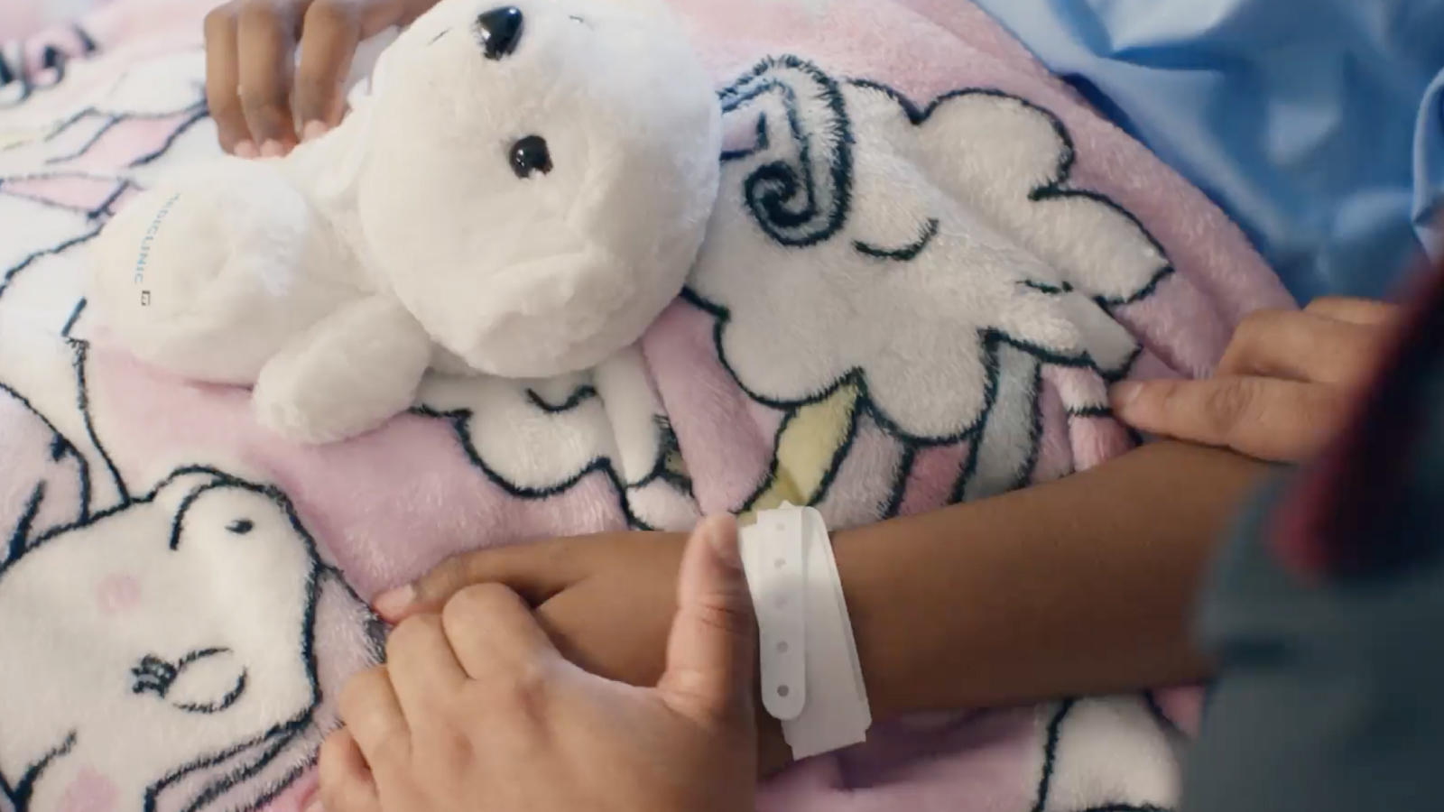 Closeup image of a young patient holding a bear and their parents hand