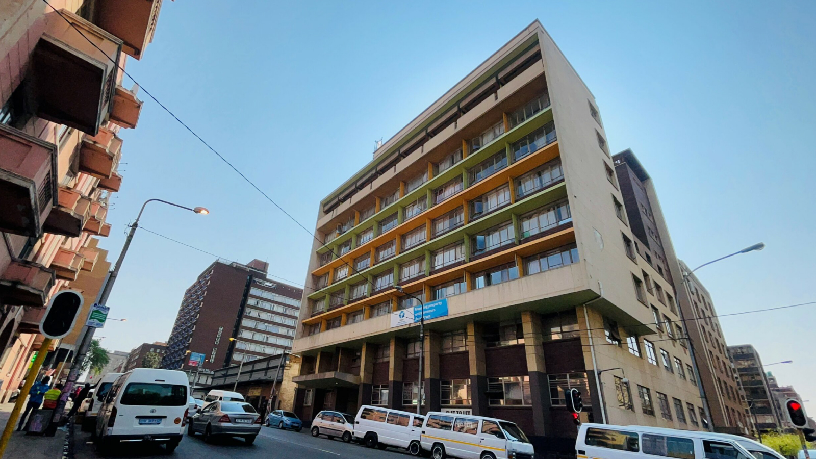 A city street with a mid-rise building, featuring colorful balconies and urban activity.