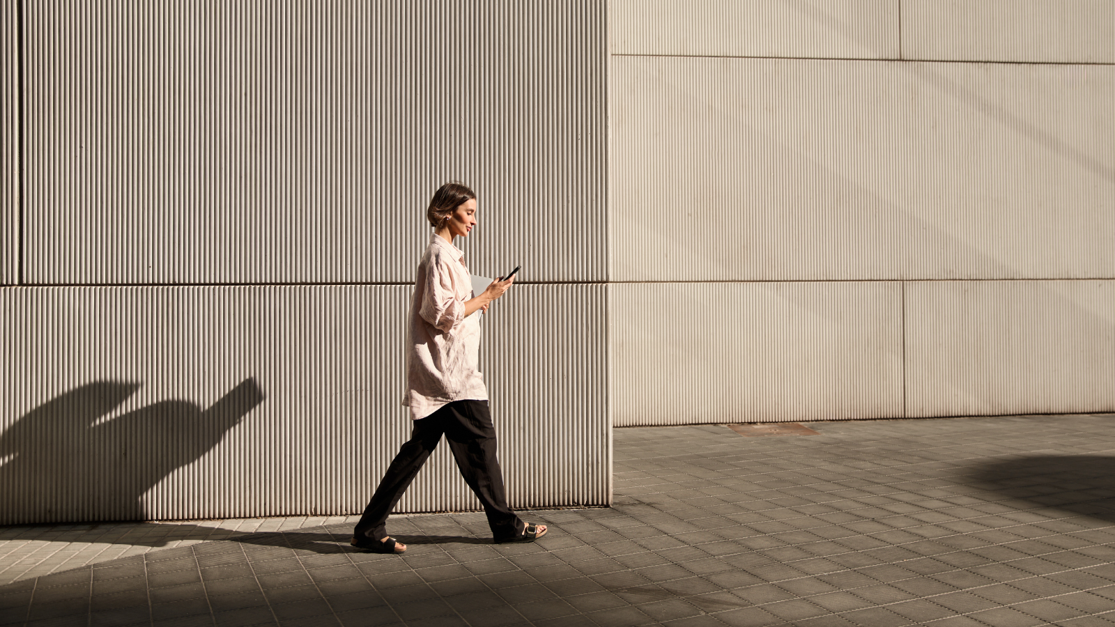 A woman strolling along the street, engaged with her phone, surrounded by urban scenery.