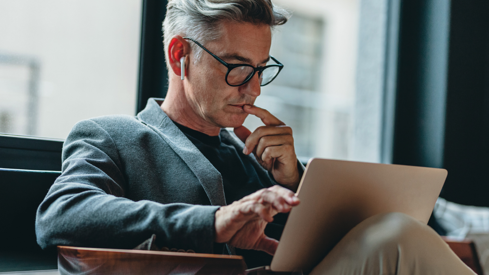 A man in glasses is at a table, using a laptop, showcasing a scene of productivity and focus.