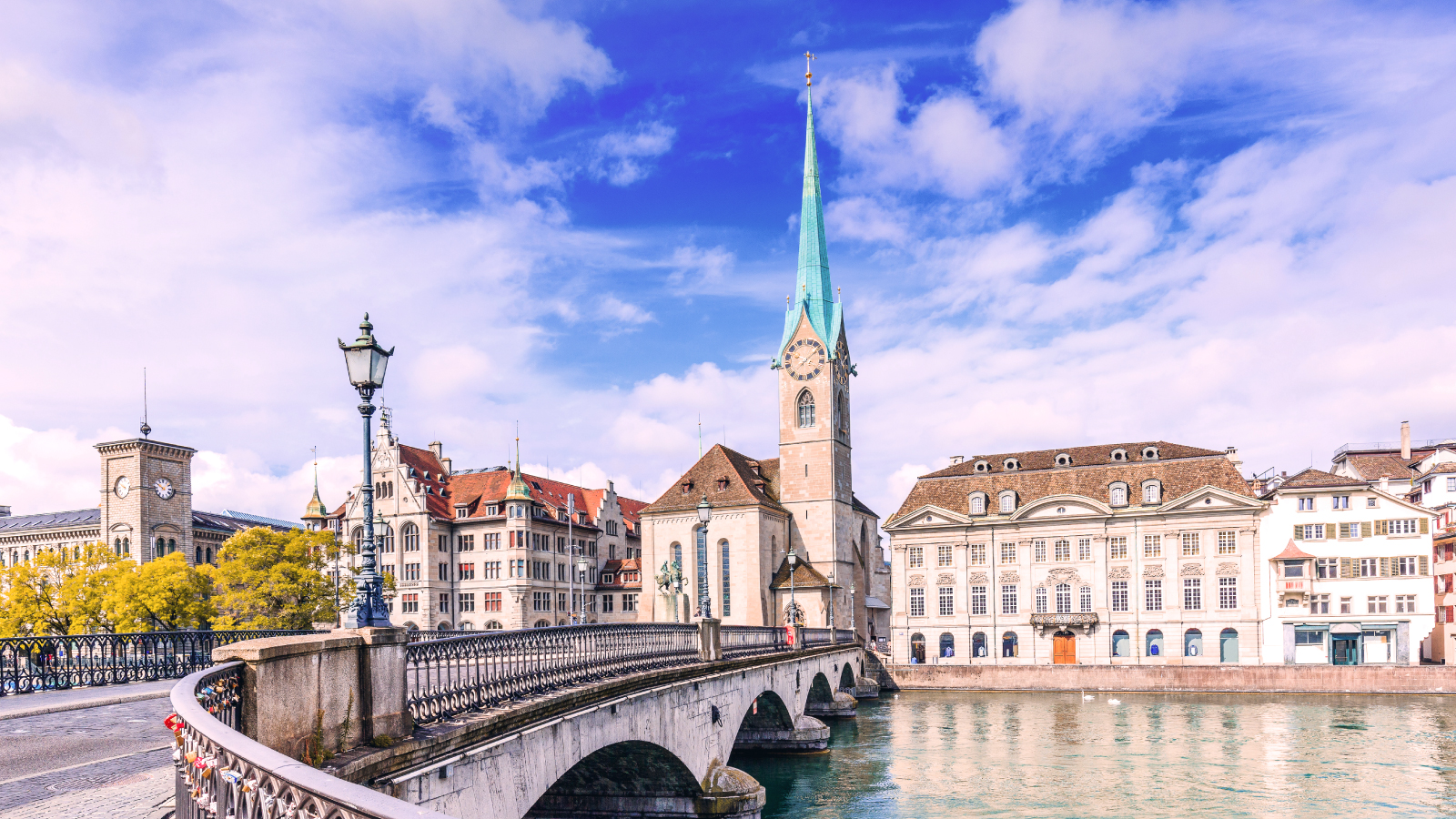 Zurich bridge, church spire, and historic buildings by the river under a blue sky.