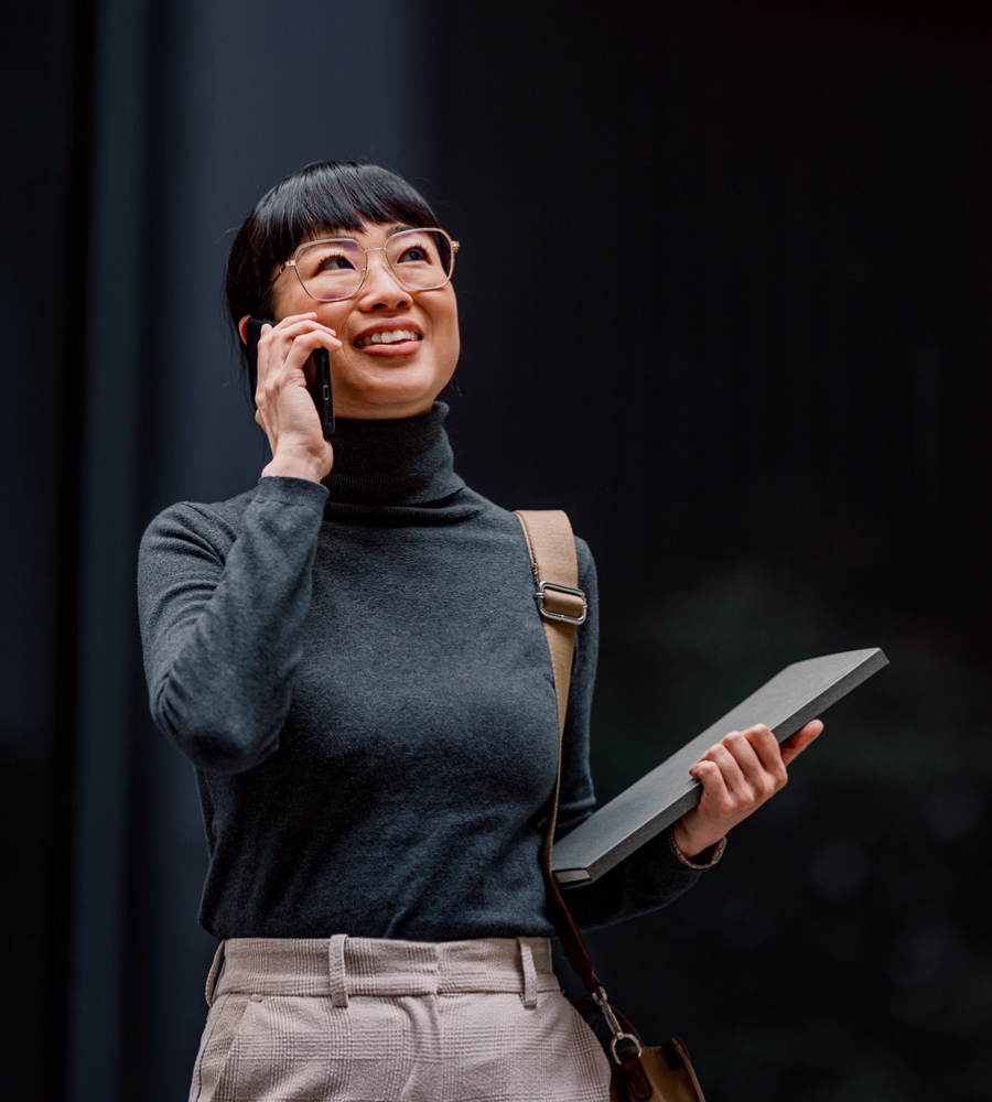 Woman holding a laptop while walking and smiling and talking on the phone