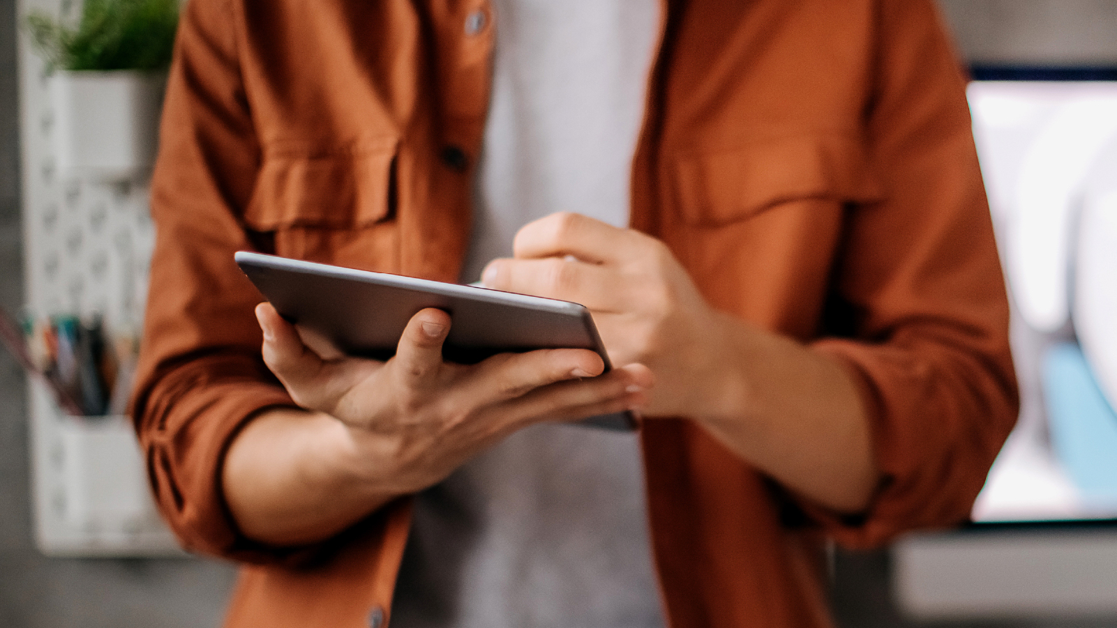 A man grips a tablet computer in one hand, appearing engaged with the device as he looks at the display.