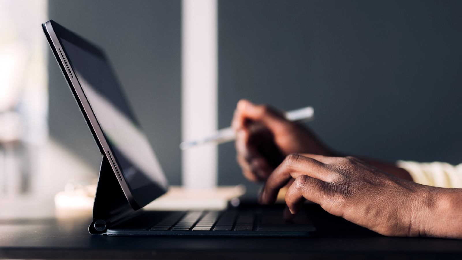 A person focused on typing on a laptop computer, with hands positioned on the keyboard and a screen illuminated.