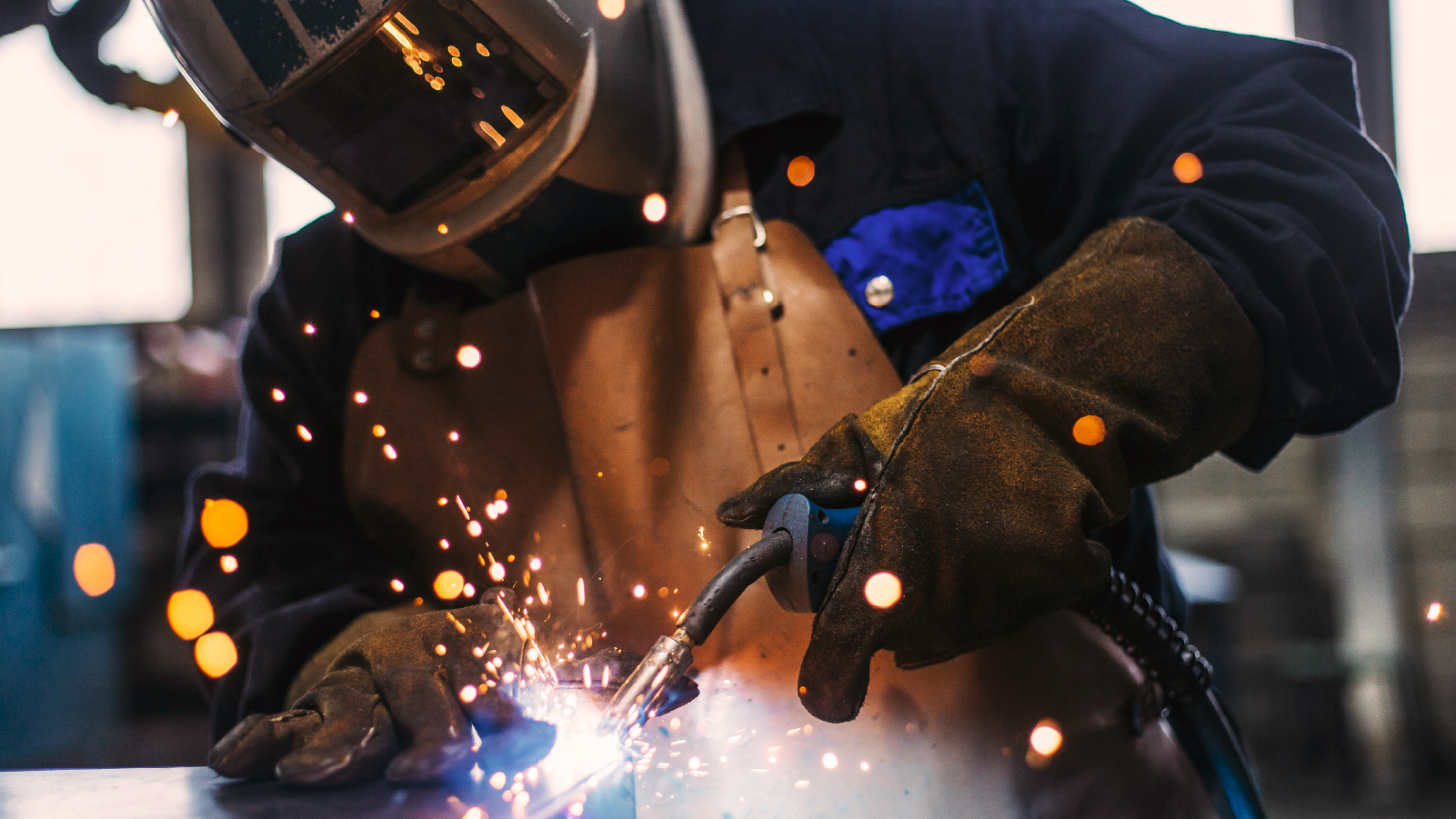 A welder engages in the process of welding metal, surrounded by sparks, demonstrating expertise in fabrication.