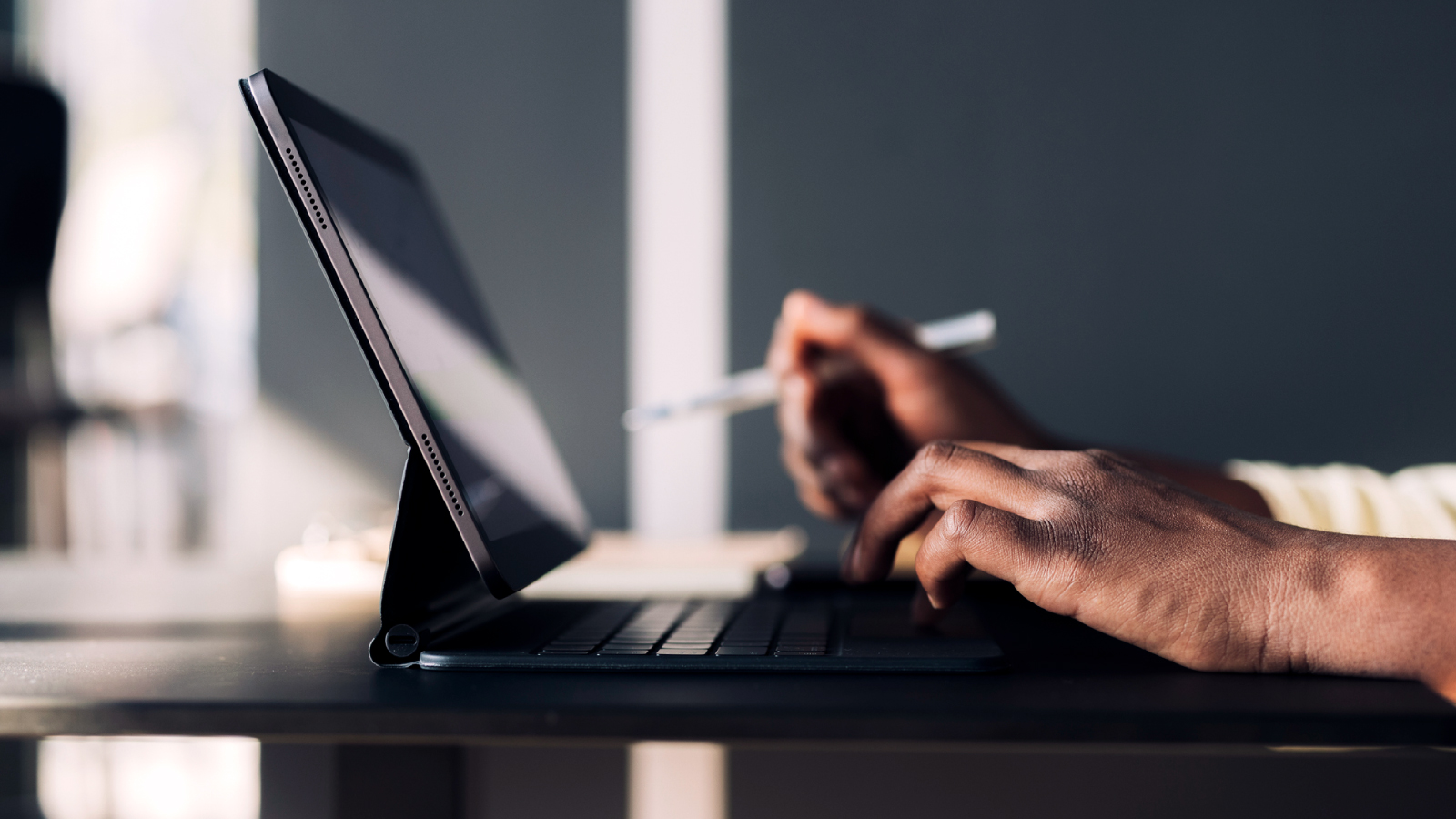 Close up image of laptop and someone typing on the keyboard while also holding a pen in their right hand