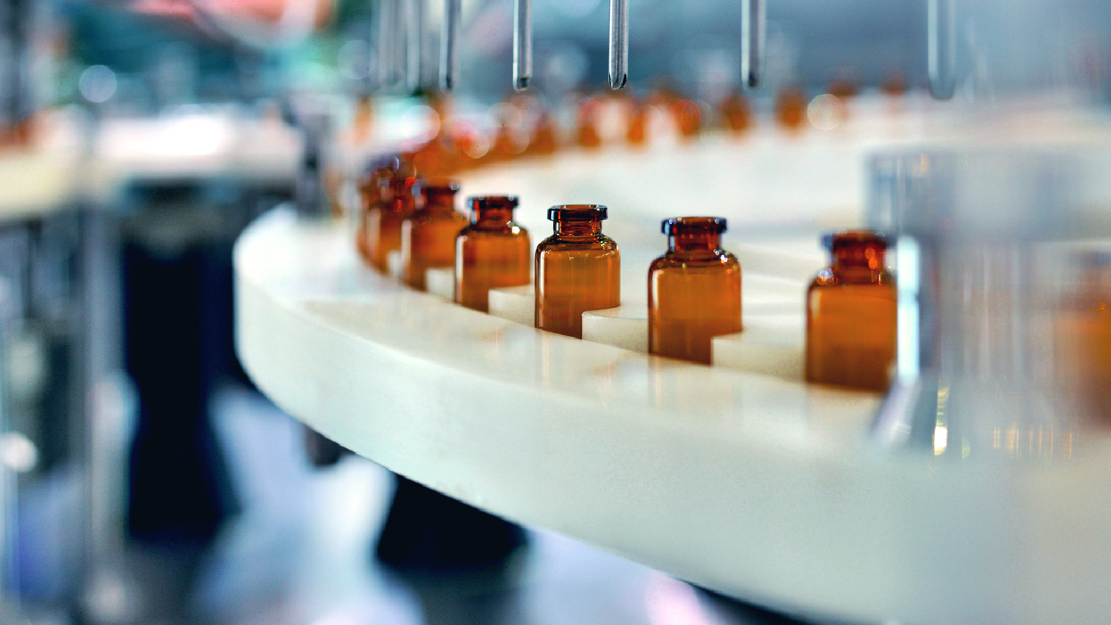 A row of medicine bottles moving along a conveyor belt in a pharmaceutical setting.