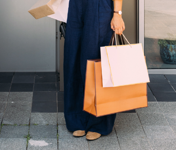 A woman in a blue jumpsuit stands confidently, holding several shopping bags in her hands.