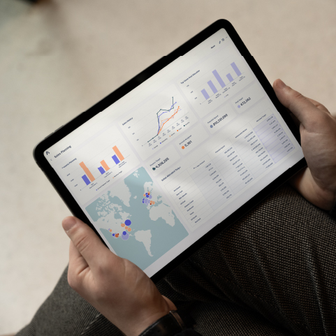 Person holding a tablet displaying a dashboard with charts, graphs, and a world map showing sales and marketing analytics.