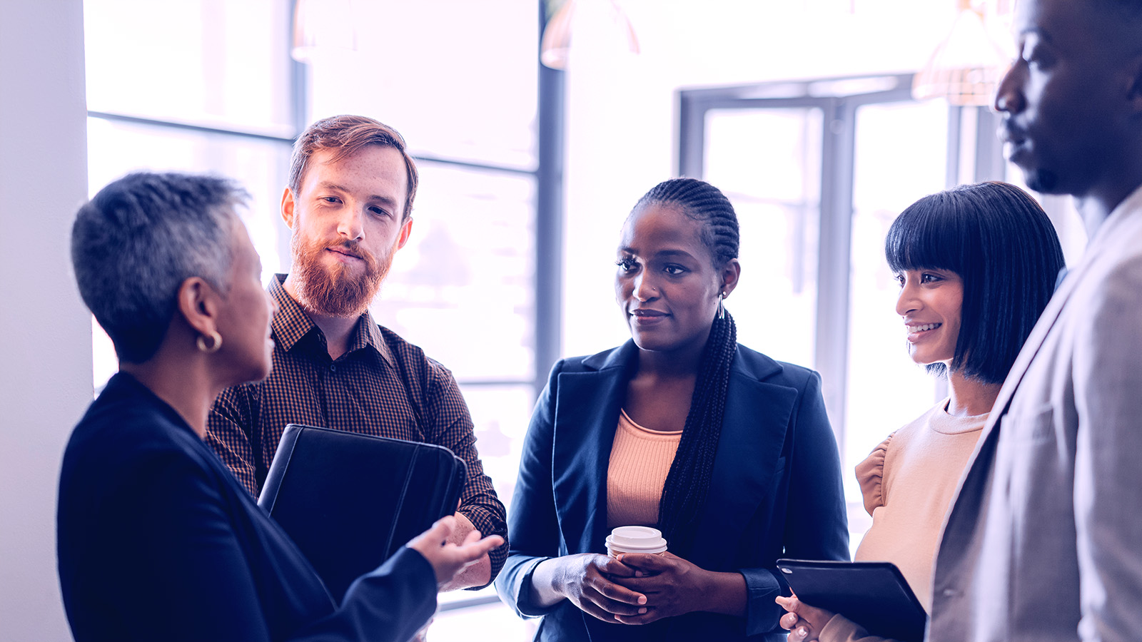 Group of coworkers standing and talking with each other while inside a well lit foyer