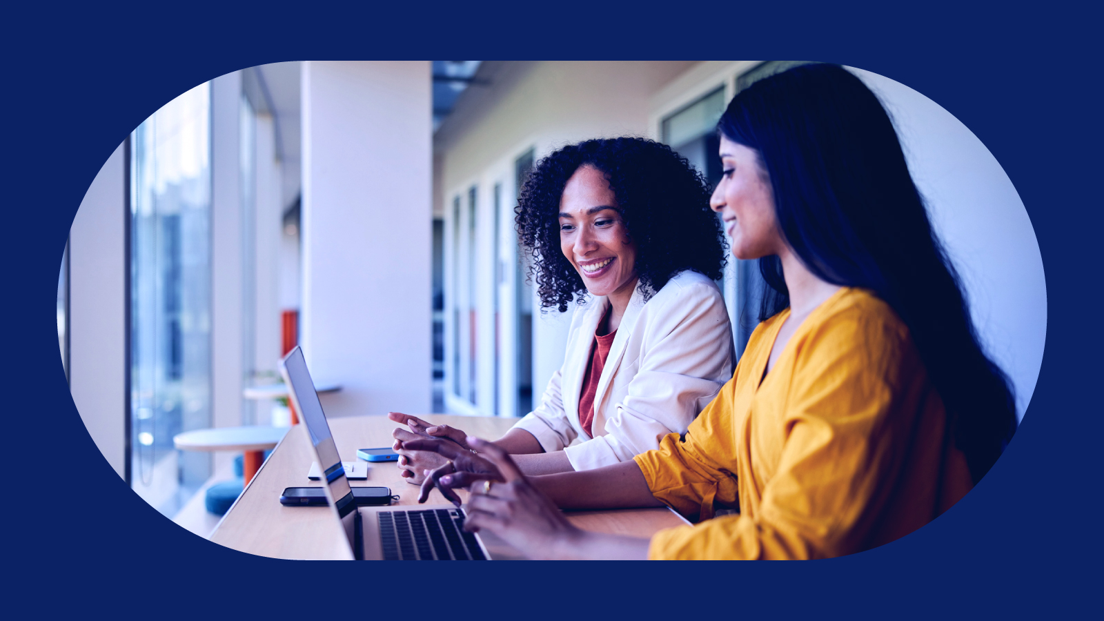 Two women smiling working on a laptop together