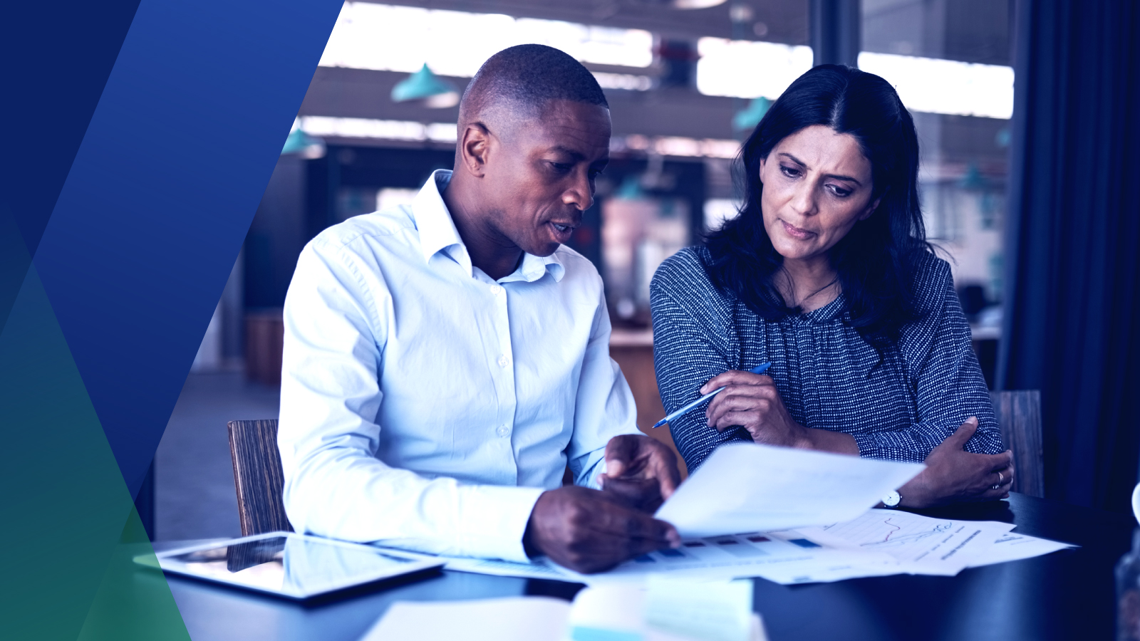 Two coworkers collaborating over financial reports at a conference table. 