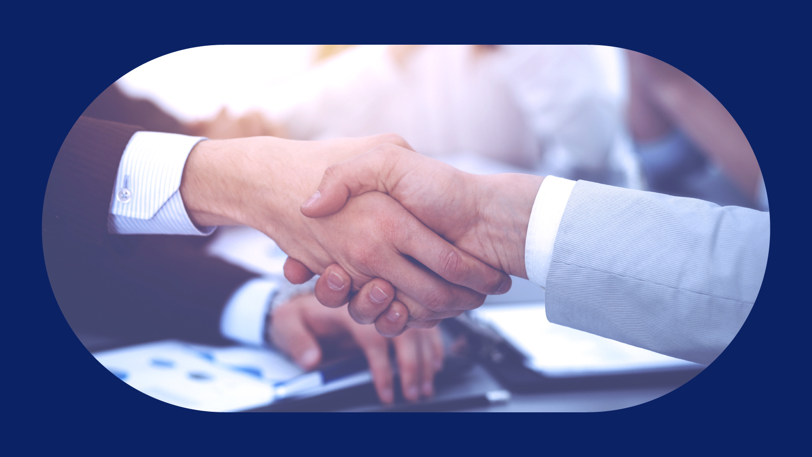 Two business individuals shaking hands across a table, representing partnership and mutual understanding in a professional setting.