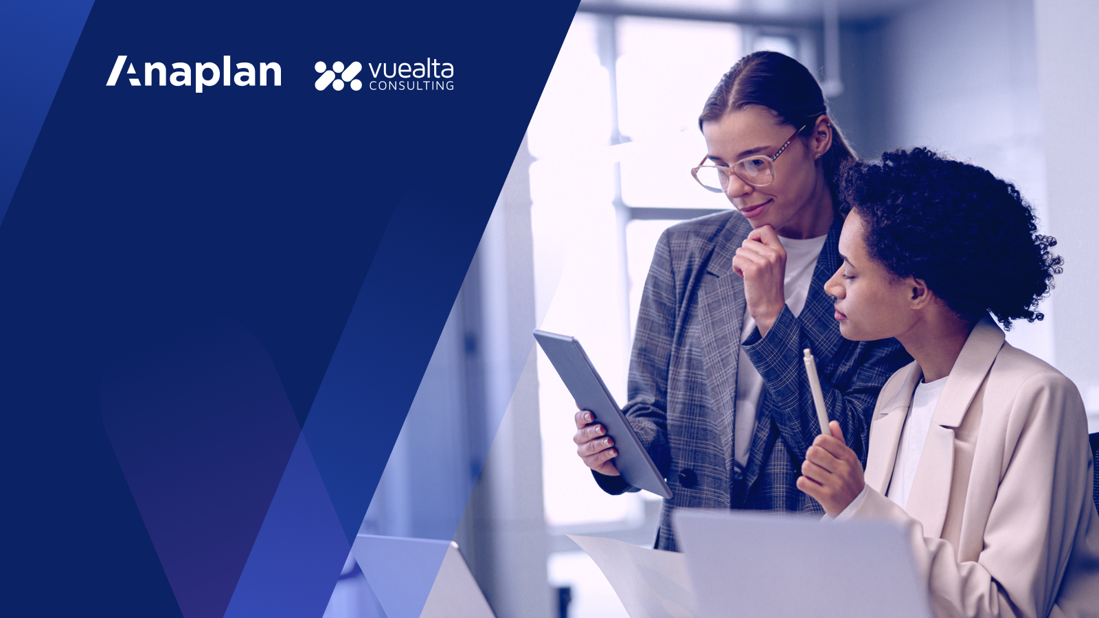 Two women in professional attire are engaged in discussion while examining a tablet together. With Anaplan and Vuelta Consulting logo