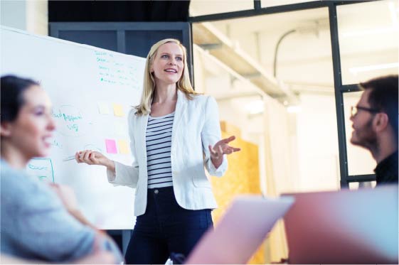 Woman presenting to coworkers in front of dry erase board